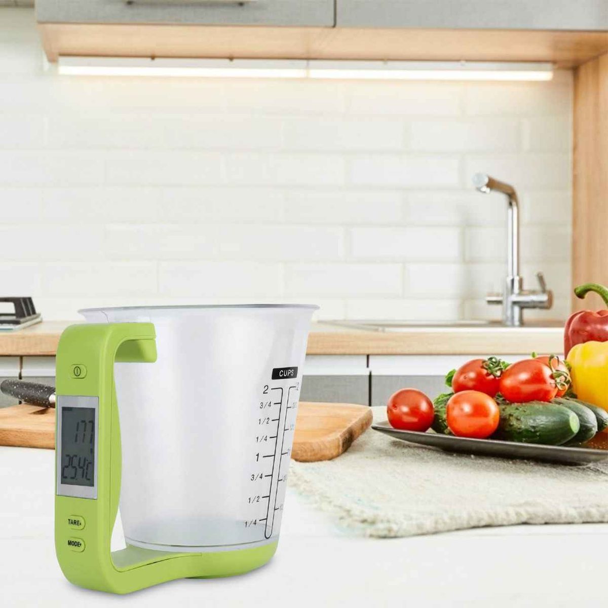 Balance de cuisine verte avec tasse mesureuse posée sur un plan de travail en bois dans une cuisine lumineuse avec des légumes frais en arrière-plan.