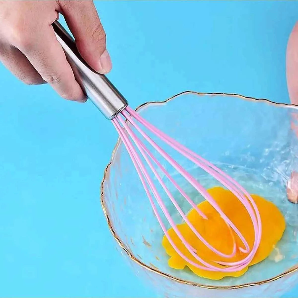 Utilisation du fouet de cuisine rose en silicone et inox pour battre des œufs dans un bol, idéal pour des mélanges homogènes sans rayer les récipients.