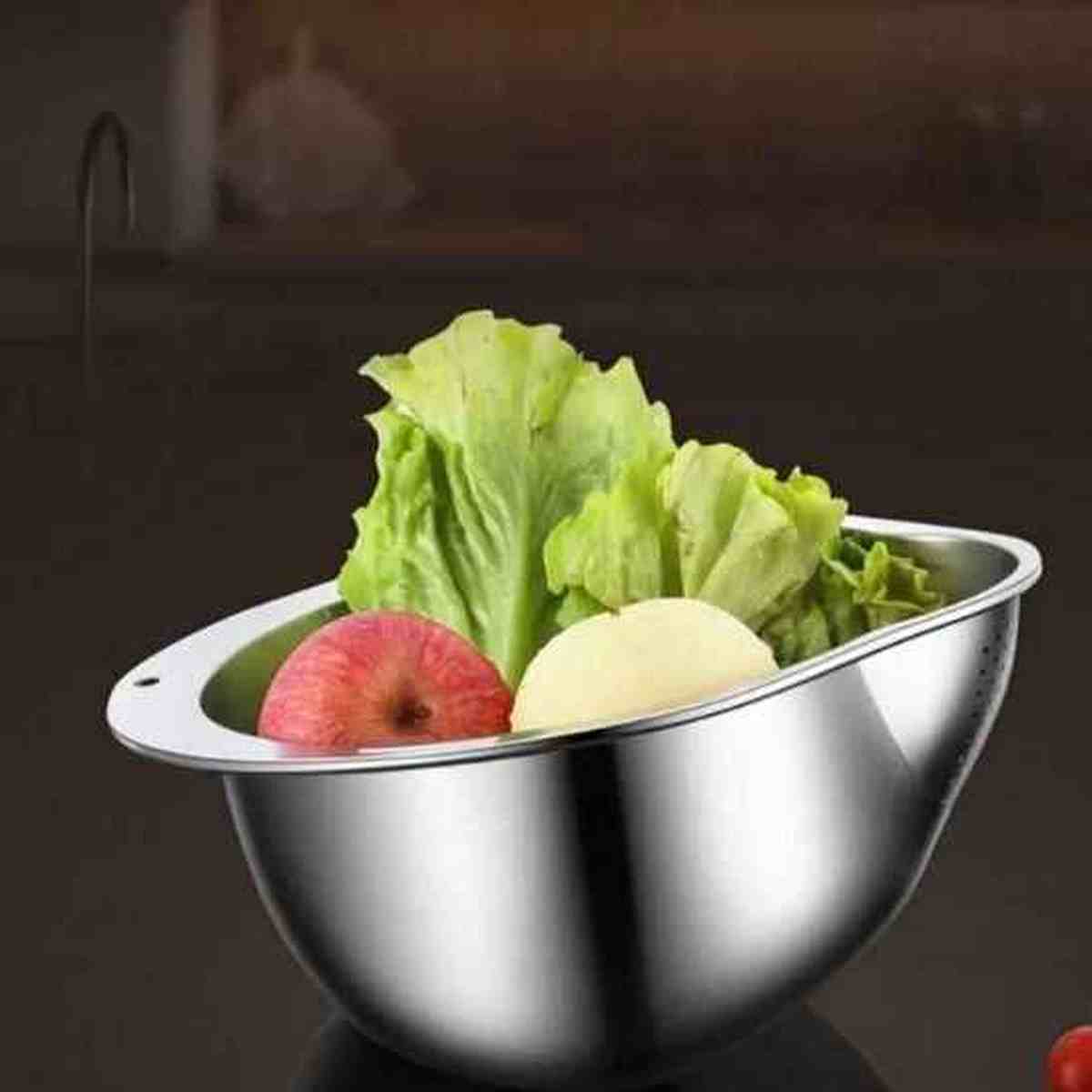 Passoire ronde en acier inoxydable brillant remplie de feuilles de salade et d'une pomme rouge, vue de profil.