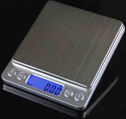 Balance de cuisine en acier inoxydable brossé avec écran LCD bleu affichant 0.00 et boutons de commande pour la fonction Tare et conversion d'unités.