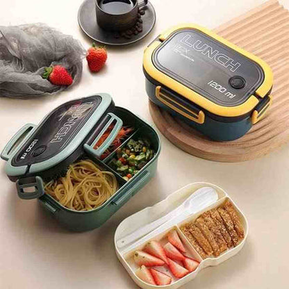 Vue de dessus d'une lunch box écologique verte ouverte montrant des compartiments remplis de pâtes, légumes et fraises, avec une boîte à couverts assortie