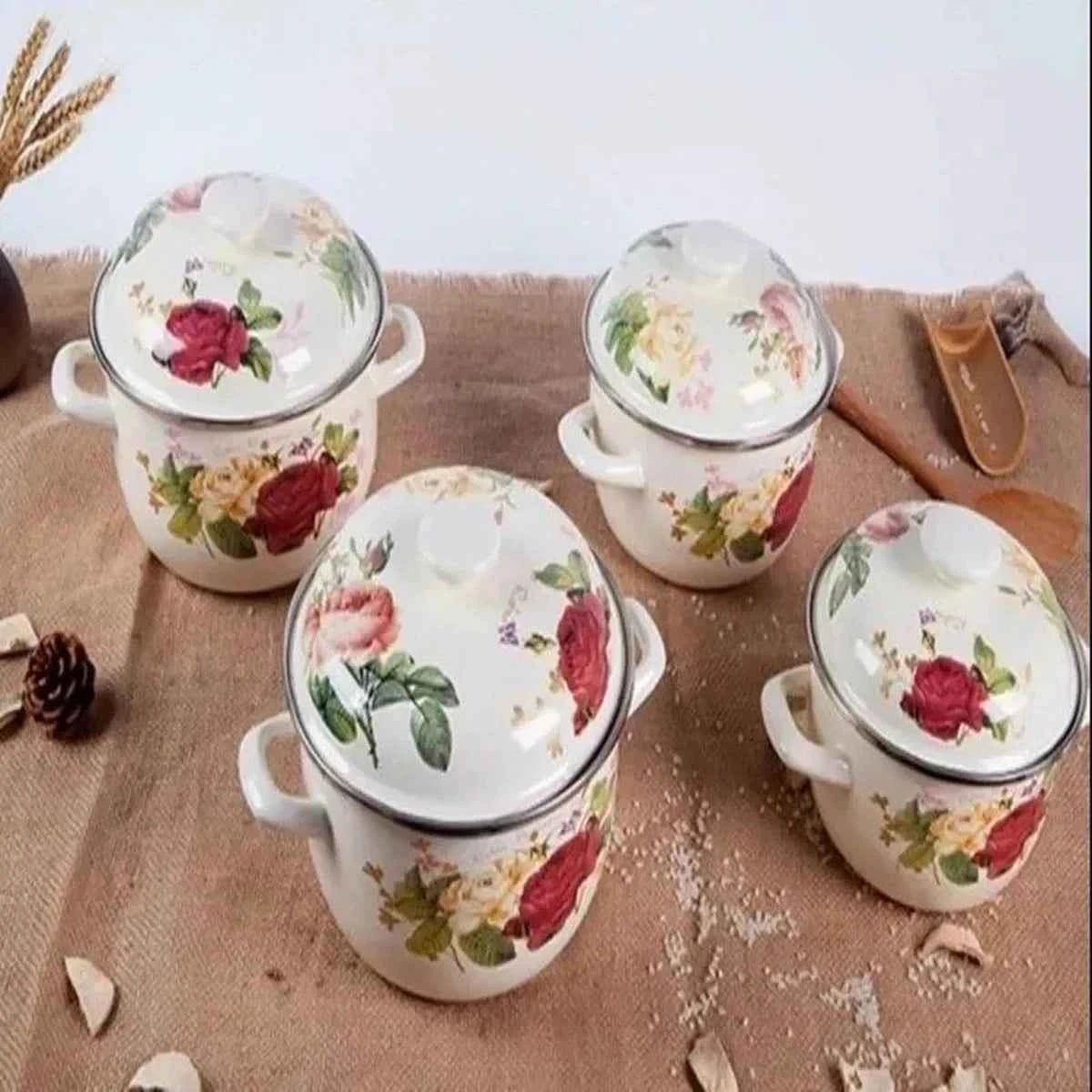 Ensemble de casseroles en céramique émaillée blanche avec couvercles, ornées de motifs floraux roses rouges, disposées sur un plan de travail.