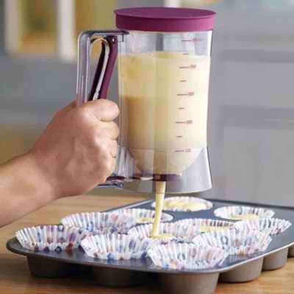 Gros plan d'un entonnoir à piston transparent avec graduations de mesure, remplissant proprement des caissettes à muffins dans un moule à pâtisserie.