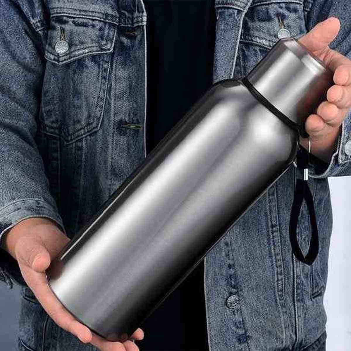 Gourde isotherme premium en acier inoxydable noir et argent posée sur un bureau avec un livre, style moderne et élégant.