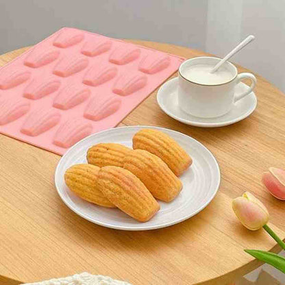 Moule à madeleines en silicone rose 12 empreintes PâtissiPro présenté dans un décor de goûter avec une assiette de madeleines fraîches et une tasse de café.