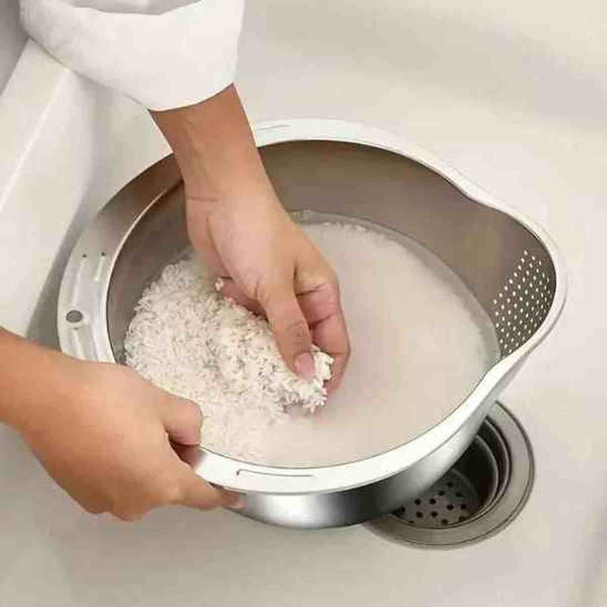 Main mélangeant du riz dans une passoire en acier inoxydable au-dessus d'un évier pour montrer la finesse des perforations.