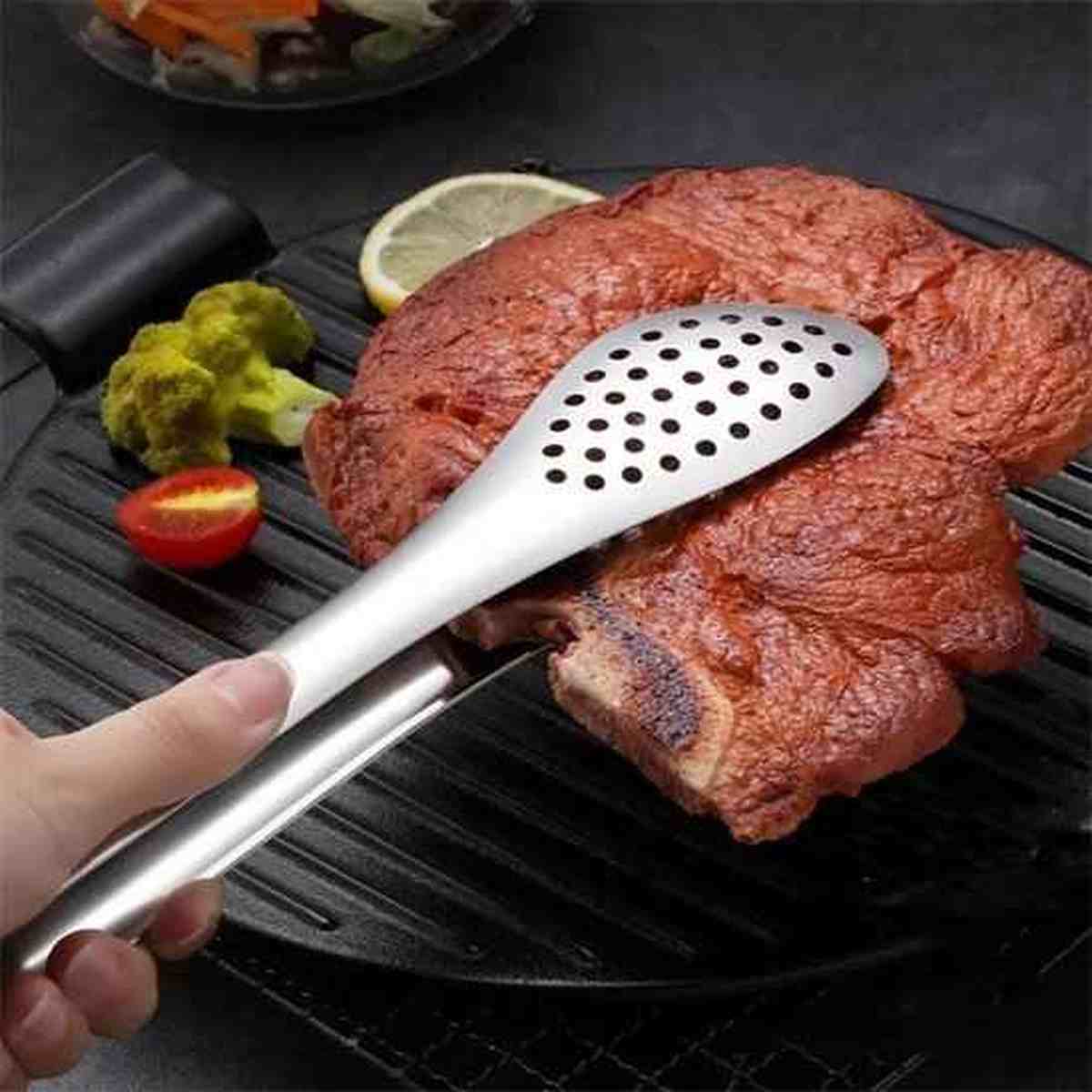 Détail d'une pince de cuisine en acier inoxydable avec tête perforée pour égoutter les aliments lors de la cuisson ou du service.
