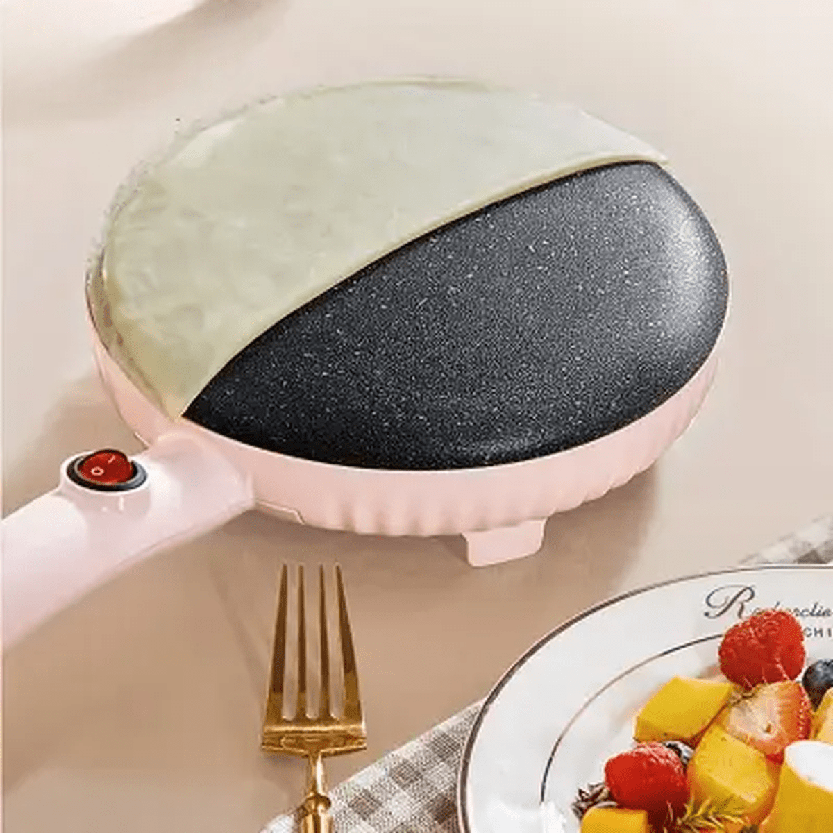 Gros plan sur la surface de cuisson noire antiadhésive de la crépière rose PancakeMaker avec une crêpe fine et une assiette de fruits frais