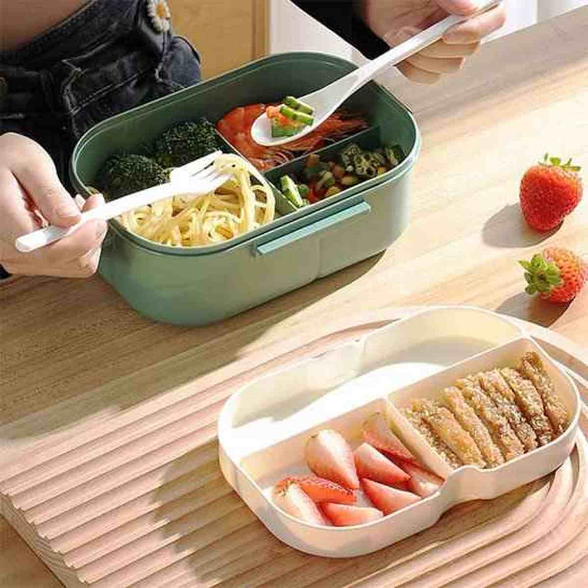 Présentation des deux plateaux amovibles de la lunch box éco-étanche, l'un contenant des pâtes et des brocolis, l'autre des fraises et de la viande grillée