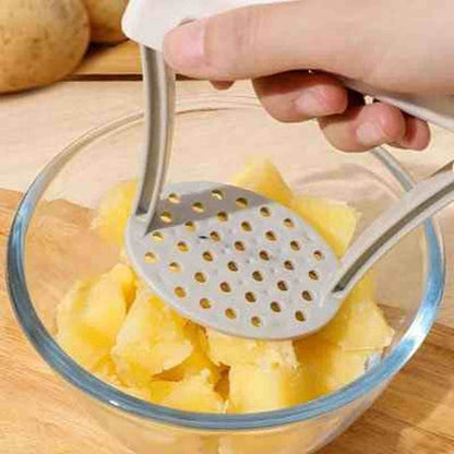 Gros plan sur la grille en acier inoxydable d'un presse-purée écrasant des pommes de terre cuites dans un bol en verre