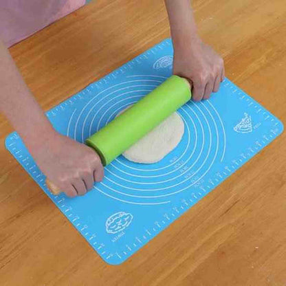 Utilisation d'un rouleau à pâtisserie en silicone vert avec poignées ergonomiques pour étaler une pâte sur un tapis de cuisson bleu.