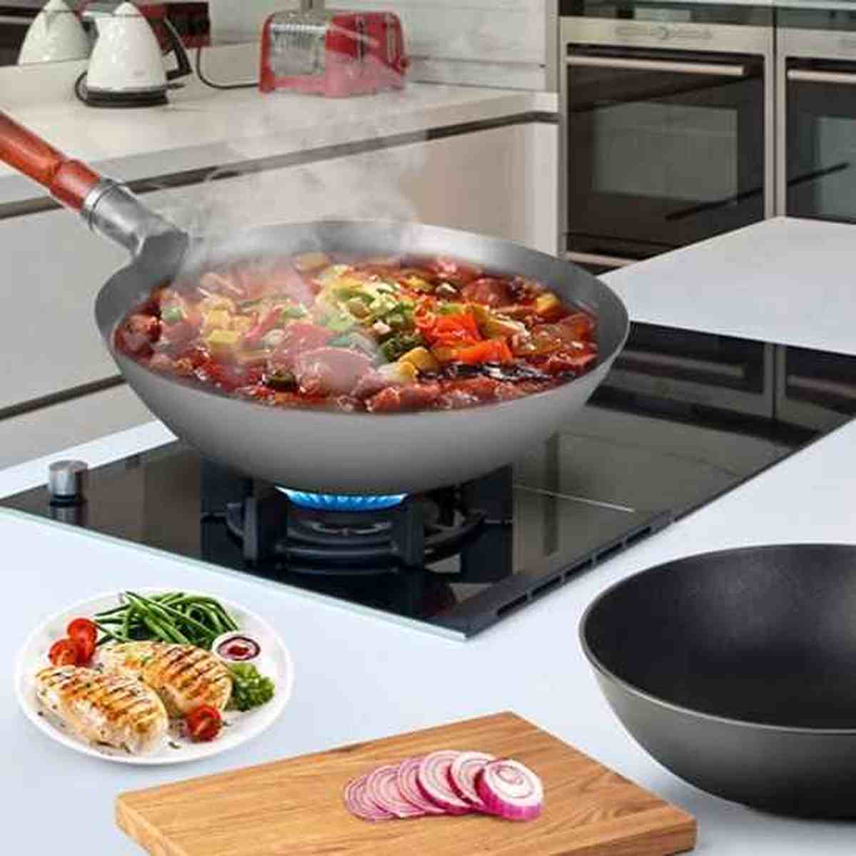 Wok professionnel en acier au carbone en cours de cuisson sur gaz avec une assiette de poulet grillé et des légumes frais.